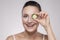 Sensitive care for luminous skin. Attractive middle aged woman looking at camera and covering eye with slice of cucumber while