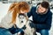 Sensitive close-up portrait of the red head woman kissing lovely siberian husky while man is stroking him. Winter time.