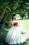 Sensitive full-length portrait of the attractive brunette bride holding and looking at the wedding bouquet of red