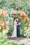 Sensitive outdoor portrait of the cheerful newlywed couple hugging above the red rose arch.