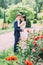 The sensitive outdoor view of the hugging newlyweds among red roses.