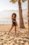 Sensual afro woman posing with palm tree on the sandy beach in Tenerife.