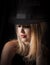 Sensual blonde woman with long hair and black fedora posing in glamor lighting