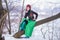 Sensual Caucasian Girl in Fashionable Green Dress and Kokoshnik with Flowery Pattern and Beads. Sitting on Tree in Winter Snowy