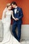 Sensual newlywed couple posing near wall outdoors in the city, wedding celebration, happy bride and groom holding hands portrait,