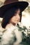 Sensual portrait of beautiful hipster woman in hat smelling  white flowers in spring. Stylish calm boho girl posing in blooming