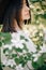 Sensual portrait of beautiful hipster woman in hat standing in white flowers in spring. Stylish calm boho girl posing in blooming