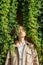 Sensual portrait of caucasian young woman with close eyes standing next to the wall of green wild grape leaves.