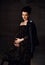 Sensual pregnant noble woman in black off-shoulder dress and leather jacket stands holding hand at her belly, feeling love