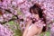 Sensual, seductive, portrait of a sexy, young, brunette woman in white dress in pink flower tree blossoms in april spring