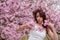 Sensual, seductive, portrait of a sexy, young woman in white dress in pink flower tree blossoms in early april spring awakening