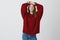 Sensual self-assured european female in red loose sweater stretching looking flirty and sassy at camera, squinting