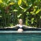 Sensual young woman relaxing in outdoor spa infinity swimming pool surrounded with lush tropical greenery of Ubud, Bali.