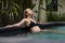 Sensual young woman relaxing in outdoor spa infinity swimming pool surrounded with lush tropical greenery of Ubud, Bali.