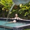 Sensual young woman relaxing in outdoor spa infinity swimming pool surrounded with lush tropical greenery of Ubud, Bali.