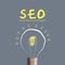 SEO concept. Search engine optimization. Glowing light bulb and word on a gray background