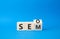 Seo and Sem symbol. Turned wooden cubes with words Sem and Seo. Beautiful blue background. Businessman hand. Business and Seo and