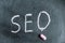 SEO. A word written in pink chalk on a black chalkboard. Handwritten text. A piece of colored chalk hangs next to it