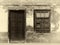 Sepia image of the facade of an old spanish house with shuttered window and old wooden door with faded plaster walls in strong s