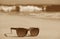 Sepia image of sunglasses on the beach with splashing waves in background