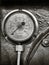 Sepia monochrome image of an old shiny brass round pressure gauge with a round dial marked in numbers on a metal panel