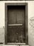 Sepia monochrome image of an old weathered wooden door nailed shut with a wooden bar and flaking paint on an outside wall