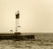 Sepia toned image of lighthouse on a pier with flying birds silhouetted
