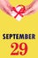 September 29th. Festive Vertical Calendar With Hands Holding White Gift Box With Red Ribbon And Calendar Date