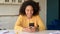 Serene African-American woman sitting at the desk at home and using smartphone