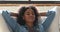 Serene african woman put hands behind head relaxing on chair