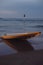 Serene beachscape with a flipped yellow kayak on sand, tranquil sea, twilight sky, and distant sailboats