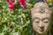 Serene Buddha face. Garden statue with fuschia flowers. Nature Buddhism