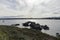 Serene Coastal View: Rocky Shoreline with a Distant Lighthouse Under a Cloudy Sky