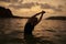 Serene dusk ocean swim. Woman stretches gracefully in calm seawater, silhouetted against amber sunset.