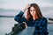 Serene girl standing alone on waterfront in front of fence of embankment