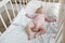 Serene infant in pink clothes lying on white linens in crib