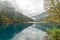 The serene Long Lake mirrors the autumnal beauty in the misty morning at Jiuzhaigou, China, creating a harmonious reflection of