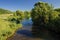 Serene sunny summer landscape. Small river with green meadows an