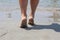 Serenity in Motion: Female Feet Stroll Towards Seawater on a Sunny Beach Day