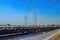 a series of flat-car trains speeding by against the backdrop of high-voltage power lines during a clear blue sky