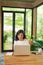 Serious adult single female sitting at table holding coffee cup and typing on laptop