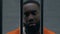 Serious African-American criminal looking at camera through prison bars, despair