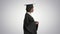 Serious African American female graduate walking with diploma on gradient background.