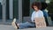 Serious African American woman black afro girl sitting on sidewalk on street near glass building near banner need work