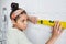 Serious African female teenager standing by white painted wall and using level measuring handtool