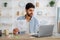 Serious arab guy looking through documents, having online business meeting on laptop while sitting at home office