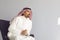 Serious arab man looks sitting while sitting on an armchair over gray background