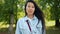 Serious Asian lady standing outdoors in green park looking at camera