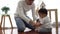 Serious Asian little boy crawling on floor while young father sitting next to him in living room