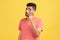 Serious bearded man in red striped t-shirt standing, holding magnifying glass and looking at camera with big zoom eye, verifying